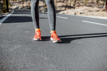 Fototapeta na wymiar Sports woman in running shoes standing on the asphalt mountain road, close-up on sneakers