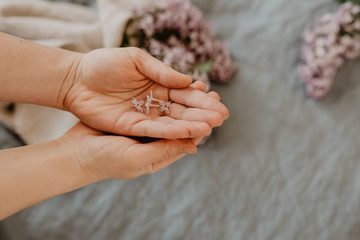 Close-up of hands holding purple lilac flowers with branch in bloom on blue linen sheet with neutral linen towel in the background, eco lifestyle concept, still life