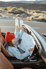 Woman traveling by convertible car on the desert valley, sitting freely on the driver's seat with...