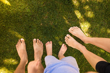 Family of three standing barefoot on grass field. 