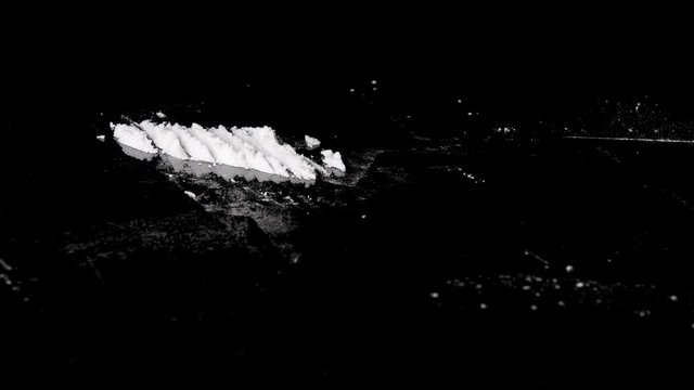 A person making cocaine powder lines with a debit or credit card, isolated on black reflective background. Close up. 