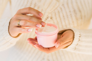 Woman holds natural white smooth cream. Cosmetic product and beauty skincare concept. Blank pink container. Close up with cream and female hands.