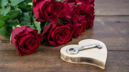 Valentine's Day background - Bunch bouquet of red roses and wooden heart with a key on rustic...