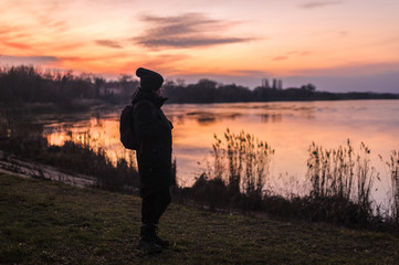 girl in winter clothes stands on a lake at sunset
