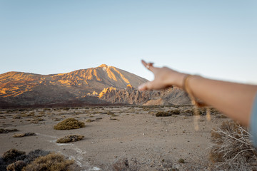 Woman pointing with hand on the volcanic mountain during a sunset, close-up on hand