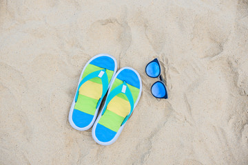Naklejka premium colorful beach shoes and blue sunglasses lie on the sea sand