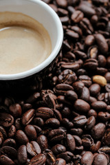cropped top view of a cup of coffee over roasted coffee beans