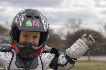 portrait of a little girl in a protective helmet and protective clothing in armor and bespalyh gloves waving a female child in a motocross helmet