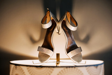 White bridal shoes on the lamp light, indoor shadows, preparation on wedding day