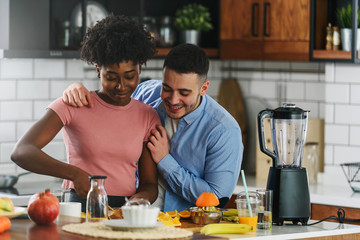 Young smiling interracial couple preparing healthy breakfast at home with lots of fruits. Healthy...
