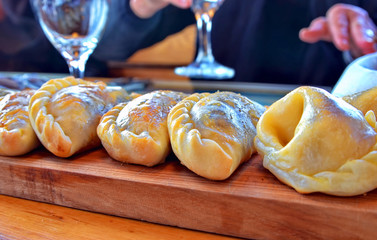 Hot baked empanadas on a traditional serving board being reached by hungry customers.