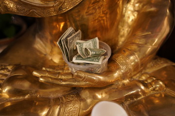 Dollar bills in a plastic container in the hand of Lakshmi, Hindu goddess of wealth, fortune and prosperity.