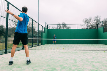 Young man playing paddle tennis on a green court, wearing a blue t-shirt.Sports concept.Copy space