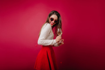 Slim young woman drinking champagne and laughing in studio. Caucasian girl in heart sunglasses...