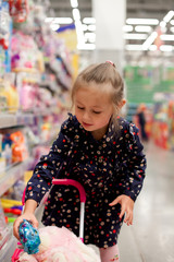 Little girl selecting toys on shelves in supermarket.
