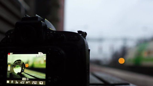 Display of camera recoding video with crystal ball reflects a passing train at station.