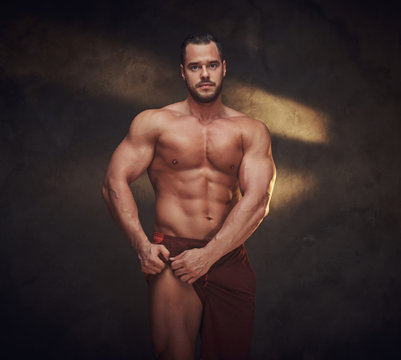 Pensive muscular bodybuilder is demonstrating his leg muscles at dark photo studio.