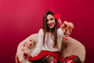 Blur portrait of long-haired girl with her hand holding heart in focus. Cute lady preparing for...