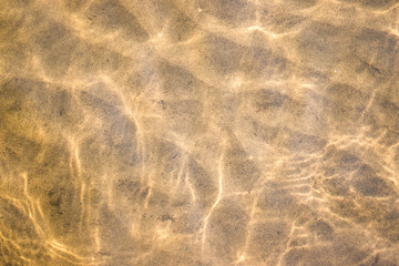Sand see through the transparent water. River water and sandy bottom background.