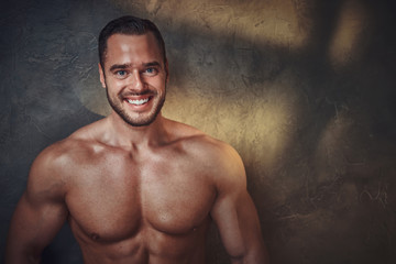 Portrait of attractive muscular bodybuilder at dark photo studio with blinks of light.