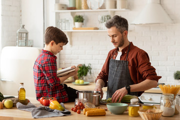 Father son cooking together by recipe in cookbook