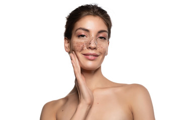 Young beautiful woman with naked shoulders applying peeling coffee scrub touching face with hands looking at camera studio portrait shot on white copy space. Scrubbing skin. Beauty procedure