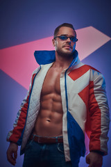 In the studio with neon background young handsome man in retro jacket has a photo session.