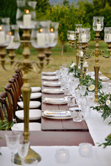 Decorated table and guest seats with floral compositions and old fashioned candlesticks outdoors in the gardens