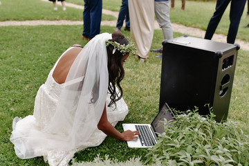 Beautiful bride is turning on music on the laptop outdoors on the grass on the wedding celebration