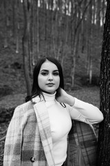 Black and white photo. Outdoor portrait of young beautiful stylish girl. Woman walking in park in warm coat, autumn fashion trend.