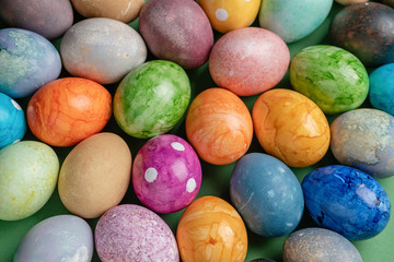 Different easter eggs with straw on wooden plate on green table