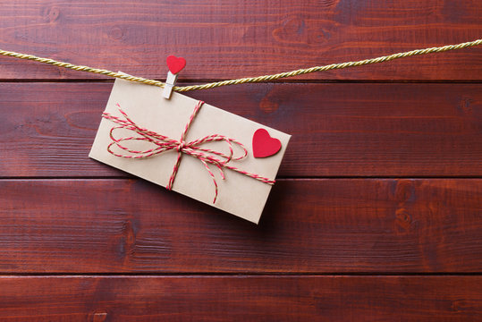 Craft envelope with red hearts hanging over wooden background. Valentines day greeting
