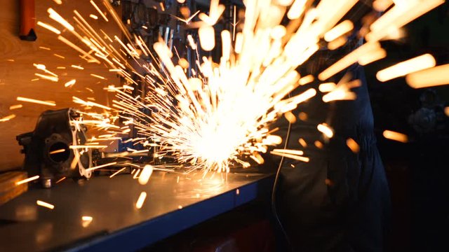 Metal worker using circular grinder. Sparks flying right in to the camera.