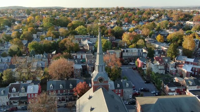 Church steeple with cross towers over Lancaster PA city, beautiful autumn fall foliage dots the urban city landscape, aerial drone shot