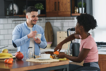 Fototapeta na wymiar Young smiling interracial couple preparing healthy breakfast at home with lots of fruits. Healthy lifestyle.