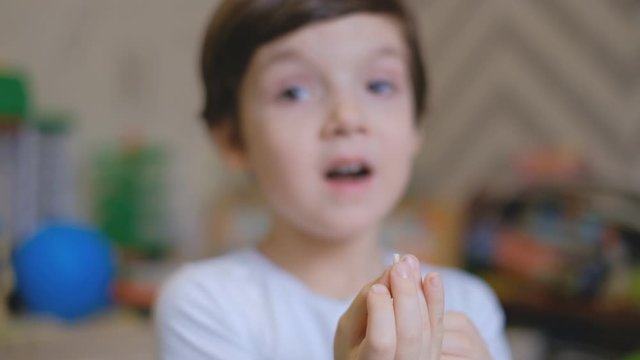 A little boy stands in a children's room and shakes his fingers a milk tooth. The boy pulls a milk tooth out of his mouth and is surprised.