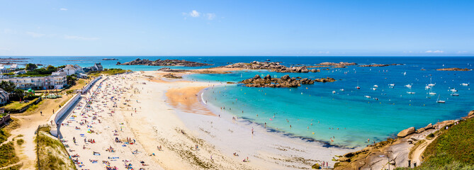Aerial panoramic view over the white sandy beach of Greve Blanche in Tregastel, northern Brittany, France, on a sunny summer day with dozens of people sunbathing and enjoying the turquoise sea. - obrazy, fototapety, plakaty