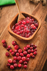 Cranberry jam in a wooden bowl on a wooden background.
