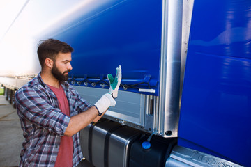Truck driver putting on gloves to remove vehicle tarpaulin for unloading. Transportation service.
