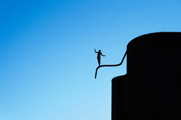 Monument to silhouette of a boy balancing on tube like tightrope walking against background of a blue sky