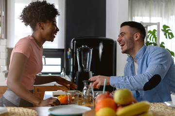 Obraz na płótnie Canvas Young smiling interracial couple preparing healthy breakfast at home with lots of fruits. Healthy lifestyle.