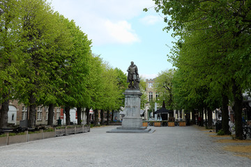 Fototapeta premium Brugge, Belgium - April 23, 2017: Statue at square in Bruges. Monument surrounded by green trees and historic buildings, springtime cityscape in Europe.
