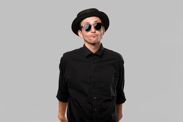 Portrait of a man in a black shirt, pork pie and sun glasses hat isolated over grey background.
