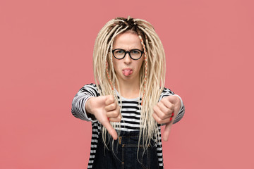 Young girl with dreadlocks in a striped shirt and jeans jumpsuit is upset holding thumbs down.