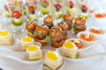 Miniburgers, canapes with pesto sauce. In the background are toasts with fried eggs, cheese and salad.
