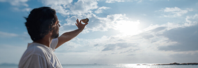 A man with a heart-shaped stone on a sunset background at the beach