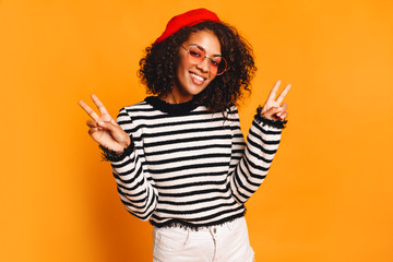 Joyful African woman posing in studio on yellow background.  Perfect smile. Copy space. peace sign...