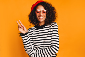 Joyful African woman posing in studio on yellow background.  Perfect smile. Copy space. peace sign...
