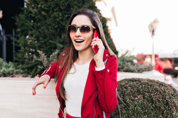 Elegant long-haired girl calling friend while walking around town. Outdoor photo of good-looking...