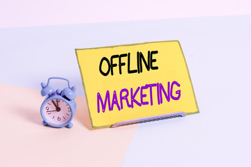 Text sign showing Offline Marketing. Business photo showcasing Advertising strategy published outside of the internet Mini size alarm clock beside a Paper sheet placed tilted on pastel backdrop